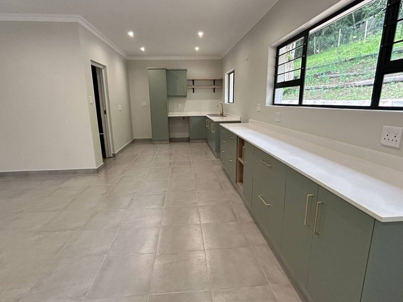 A modern, empty kitchen featuring sage green cabinetry, white stone countertops, tiled flooring, and recessed lighting, offering a clean and contemporary space.