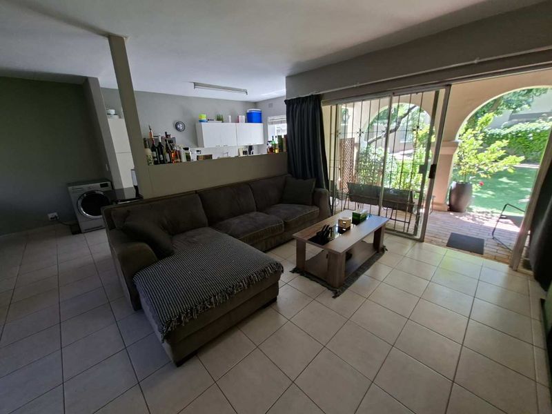 Open plan living area featuring tiled floors, built-in kitchen cabinetry, and large sliding glass doors providing direct access to a covered patio and garden.
