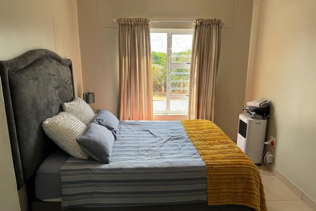 A well-lit bedroom featuring neutral wall tones, tiled flooring, and a window providing natural light.