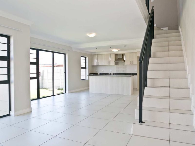 Spacious open-plan living area featuring a modern kitchen with island, tiled flooring, and a staircase with a sleek metal balustrade.