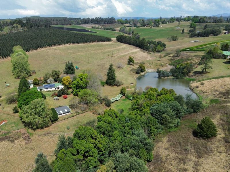 Aerial view of a rural farm property featuring a main dwelling with solar panels, surrounding pasture, mature trees, and a private farm dam.