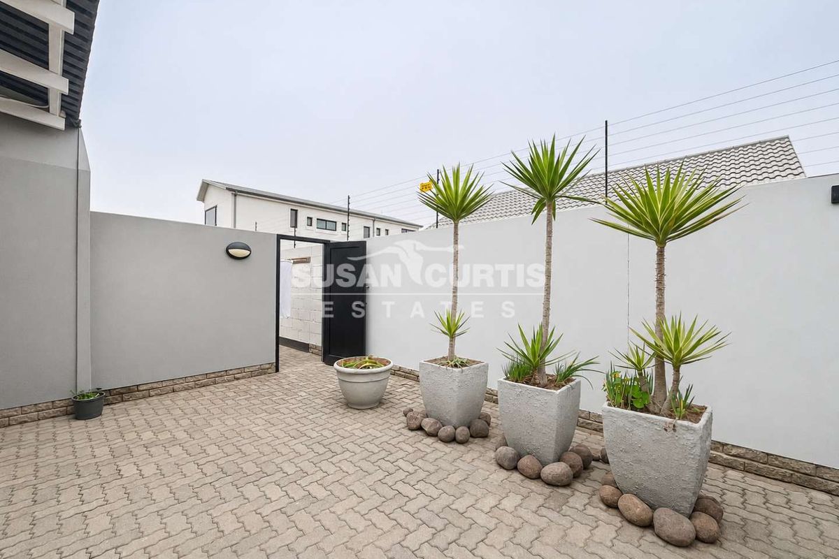 A clean, paved rear courtyard area featuring a secure pedestrian gate, boundary walls with electric fencing, and modern exterior lighting.