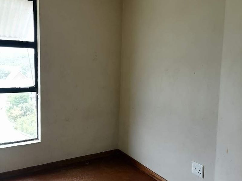 An empty bedroom featuring a metal-framed window, worn flooring, and neutral walls in need of cosmetic attention.