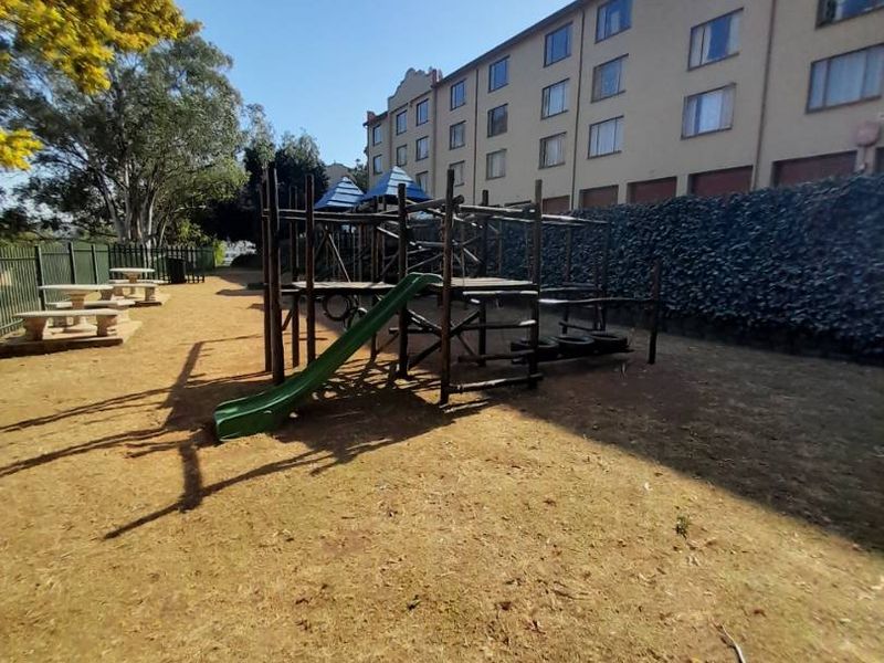 Communal garden area featuring a playground structure, perimeter fencing, and a retaining wall adjacent to the apartment building.