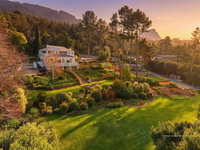 An elevated aerial view of a large, well-maintained residential property featuring extensive landscaped gardens, stone pathways, and a multi-level house set against a mountain backdrop.