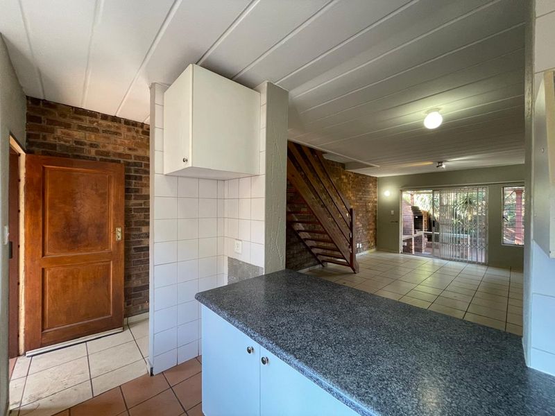 Open plan living area featuring exposed brick walls, tiled flooring, a wooden staircase, and direct access to the rear patio through sliding glass doors.