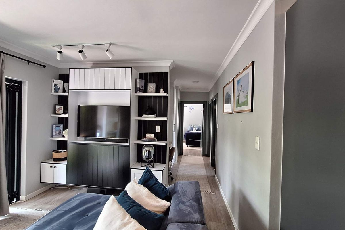 A well-maintained living room featuring custom built-in cabinetry, modern track lighting, and elegant crown molding, leading into a hallway.