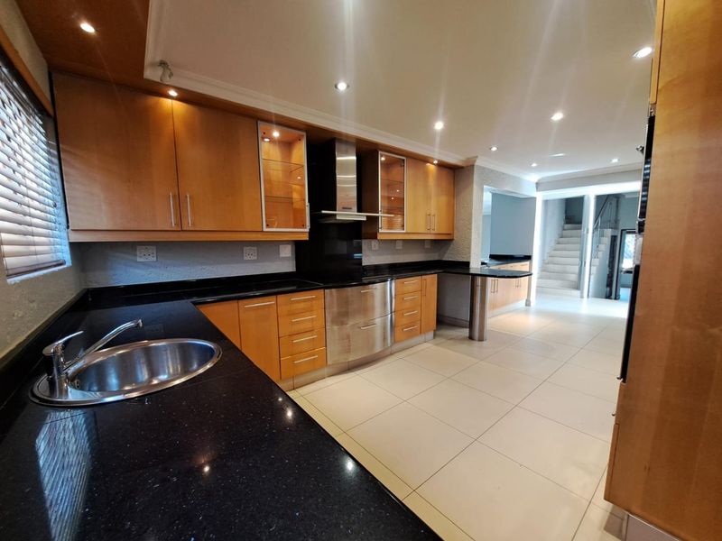 Modern kitchen featuring wooden cabinetry, black granite countertops, stainless steel extractor fan, and tiled flooring with an integrated breakfast bar.