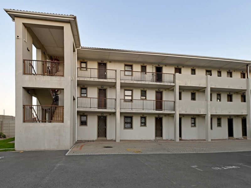 Exterior view of a multi-story apartment complex featuring external stairwells, private balconies with metal railings, and a paved parking area.