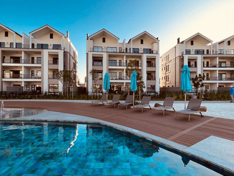 A well-maintained communal swimming pool area featuring timber decking and modern multi-story apartment buildings in the background.