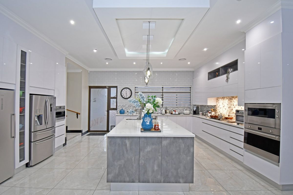 Modern, high-end kitchen featuring a central island with stone countertops, glossy cabinetry, built-in appliances, and elegant recessed lighting in a coffered ceiling.