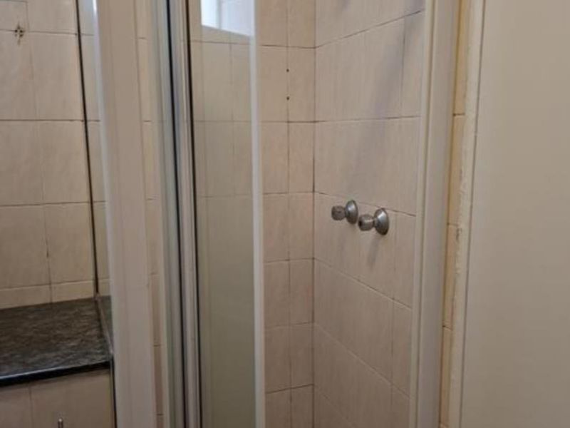 A functional bathroom featuring a glass-enclosed shower with tiled walls and a vanity countertop.