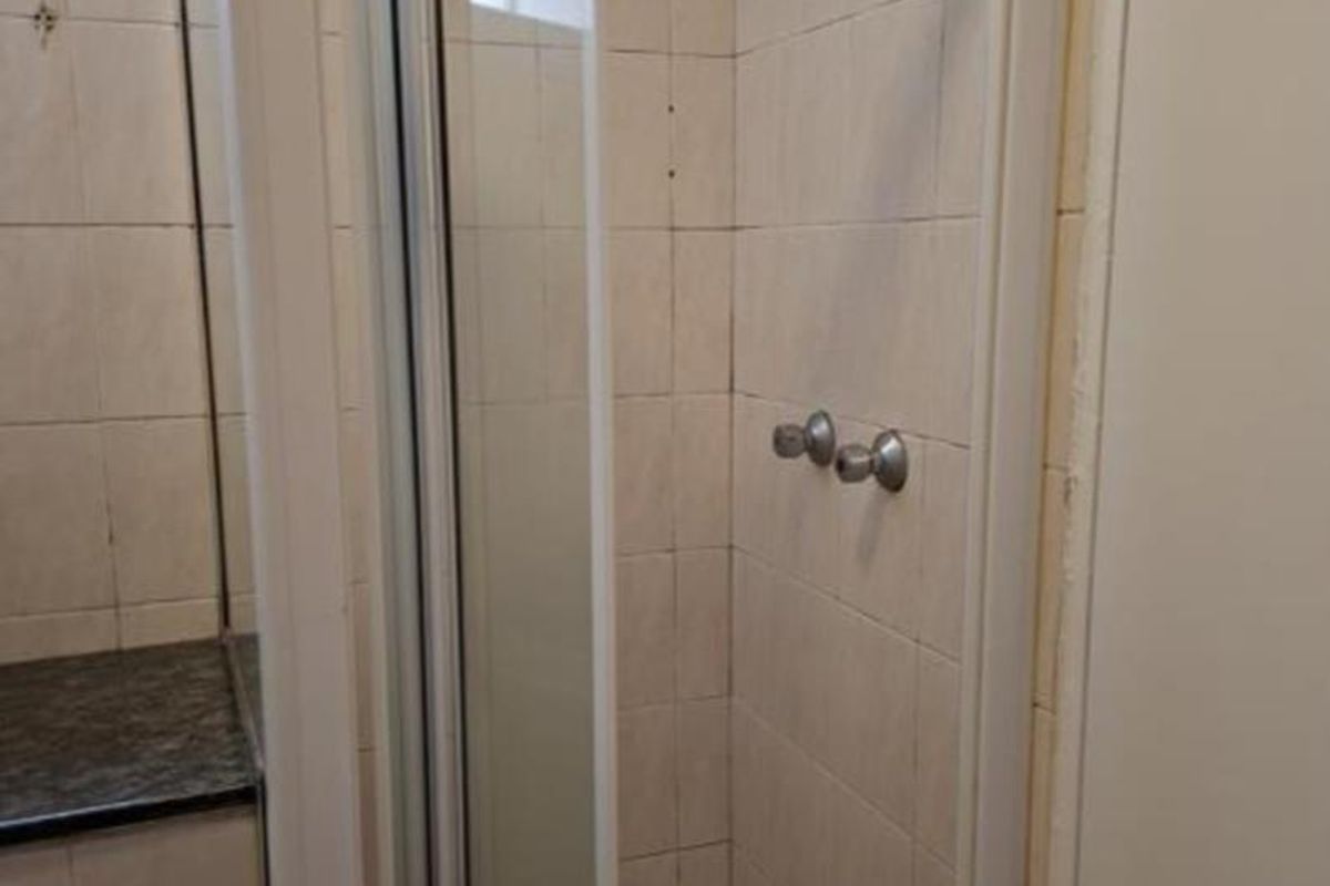 A functional bathroom featuring a glass-enclosed shower with tiled walls and a vanity countertop.