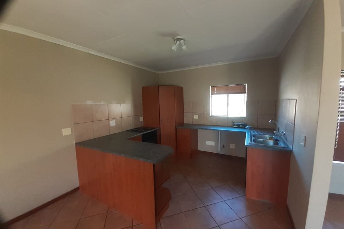 An empty kitchen featuring wooden cabinetry, laminate countertops, a double basin sink, and tiled flooring, offering a functional layout ready for personalization.