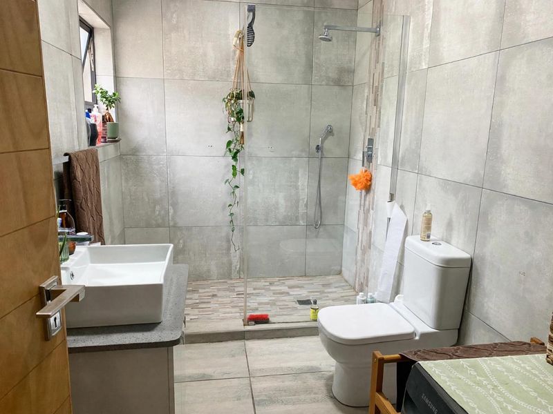 Modern bathroom featuring a walk-in shower with glass screen, vessel sink on a stone vanity, and neutral large-format wall and floor tiling.