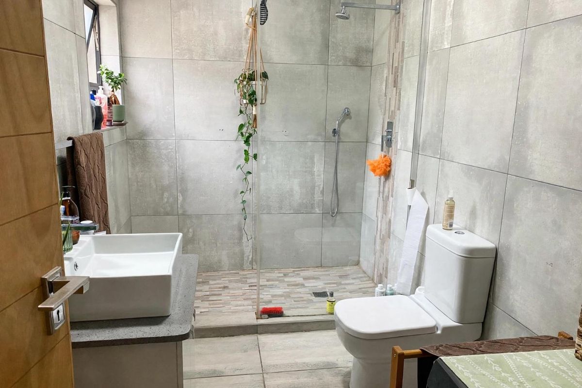 Modern bathroom featuring a walk-in shower with glass screen, vessel sink on a stone vanity, and neutral large-format wall and floor tiling.