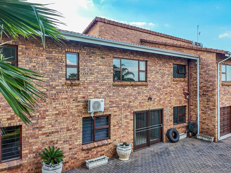 Rear view of a double-storey face brick house featuring a paved driveway, multiple aluminium-framed windows, and integrated garage access.
