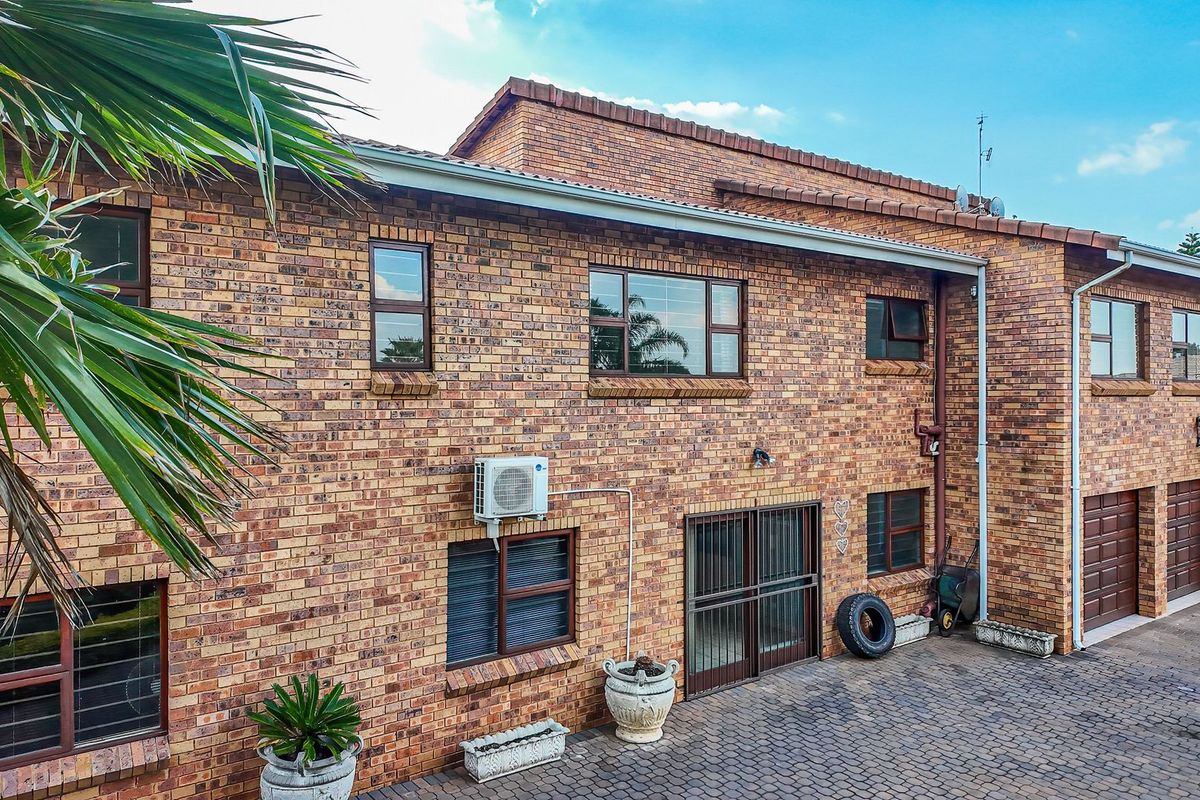 Rear view of a double-storey face brick house featuring a paved driveway, multiple aluminium-framed windows, and integrated garage access.
