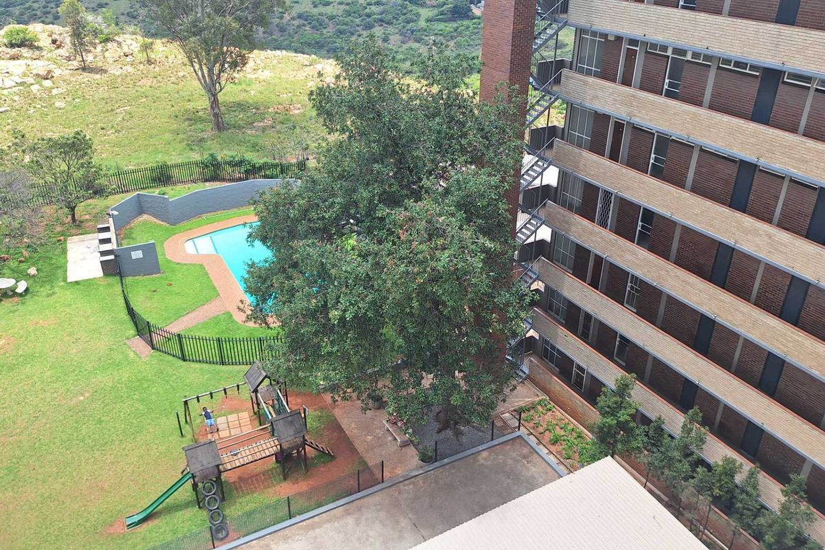 Aerial view of the apartment complex grounds featuring a swimming pool, landscaped garden areas, and secure perimeter fencing.