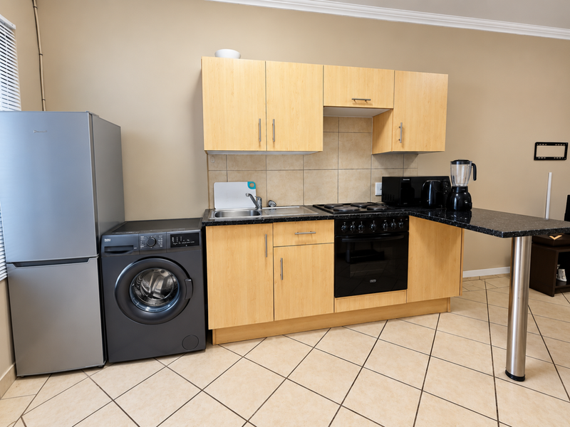 Compact kitchen featuring light wood cabinetry, dark laminate countertops, tiled backsplash, and integrated electric oven and hob with a breakfast bar extension.