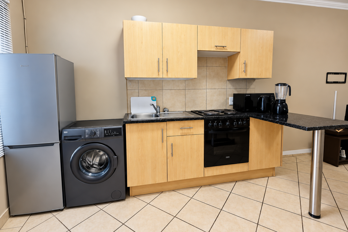 Compact kitchen featuring light wood cabinetry, dark laminate countertops, tiled backsplash, and integrated electric oven and hob with a breakfast bar extension.