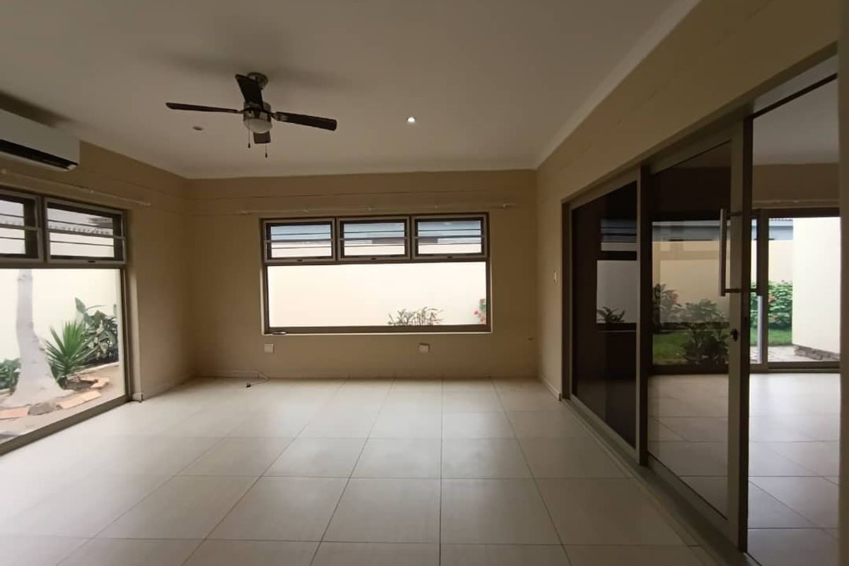 Spacious, light-filled living area featuring neutral tiled flooring, ceiling fan, air conditioning, and large sliding glass doors providing access to the outdoor space.