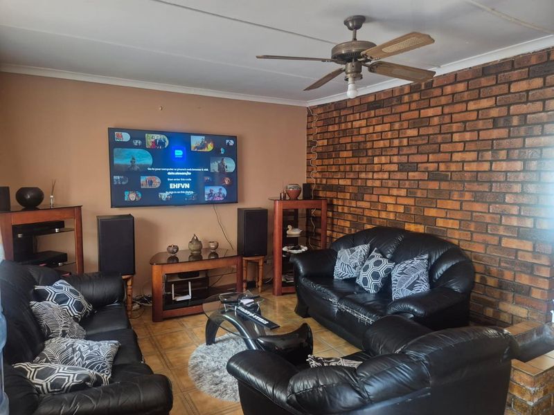 A living room featuring an exposed brick accent wall, tiled flooring, and a ceiling fan, offering a functional space with potential for modern updates.
