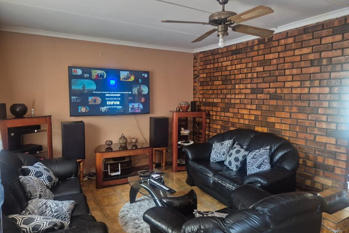A living room featuring an exposed brick accent wall, tiled flooring, and a ceiling fan, offering a functional space with potential for modern updates.