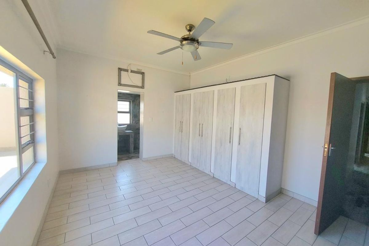 A bright bedroom featuring tiled flooring, a ceiling fan, and built-in wardrobes, with an adjoining en-suite bathroom.