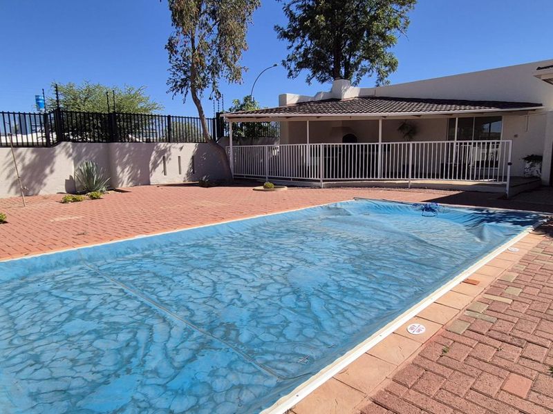 Outdoor pool area featuring a paved patio, covered veranda, and secure perimeter wall with electric fencing.