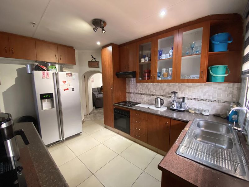 A functional kitchen featuring wooden cabinetry, laminate countertops, a double stainless steel sink, built-in oven, and electric hob with a tiled backsplash.