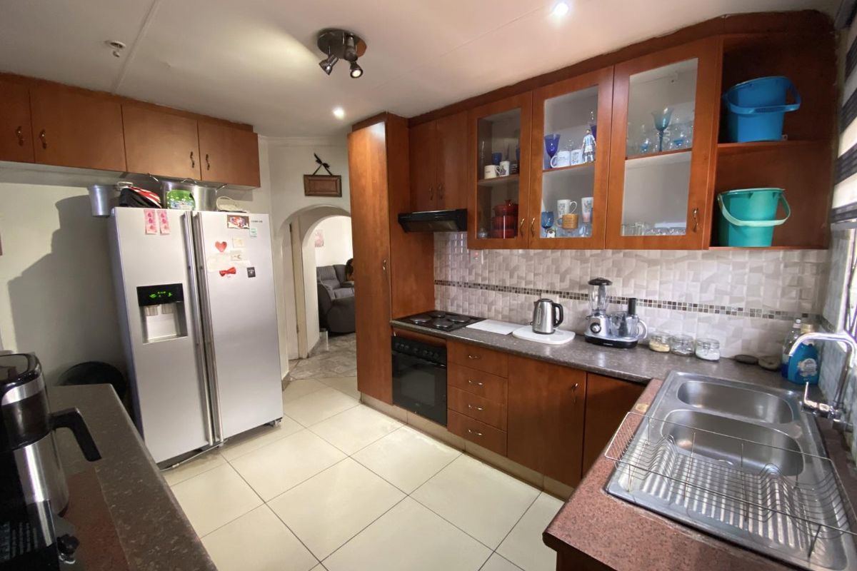 A functional kitchen featuring wooden cabinetry, laminate countertops, a double stainless steel sink, built-in oven, and electric hob with a tiled backsplash.