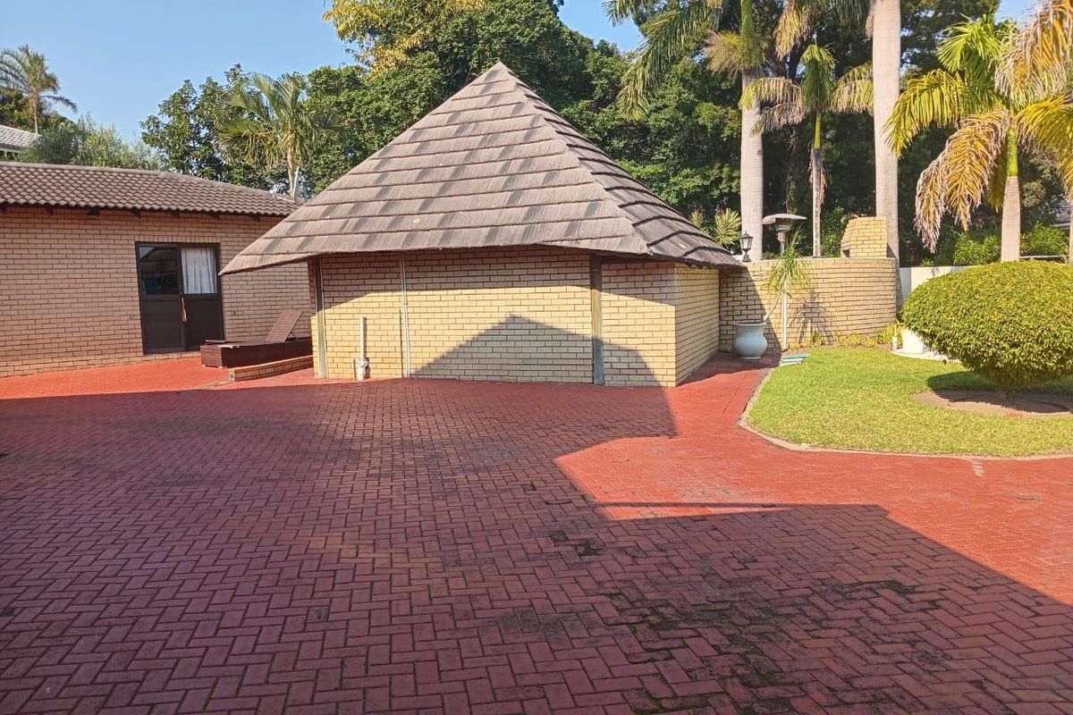 A view of the rear exterior area featuring a brick-built structure with a pitched roof, red paved driveway, and landscaped garden surroundings.