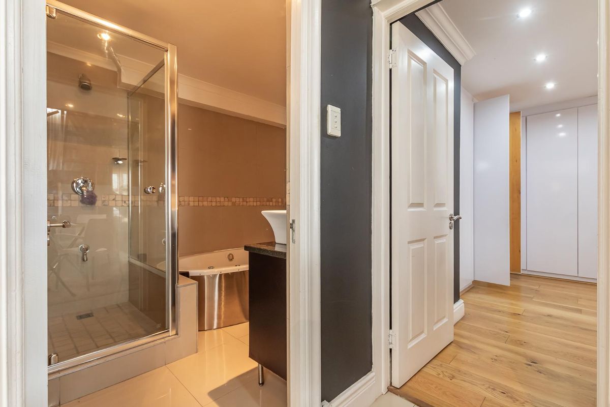 A modern bathroom featuring a glass-enclosed shower, built-in bathtub, and vessel sink, adjacent to a hallway with timber flooring and built-in storage.