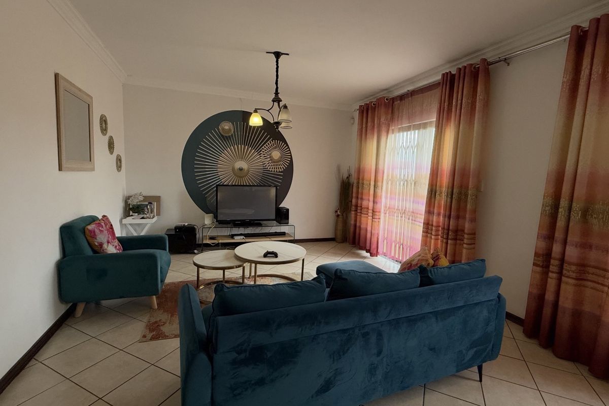 A comfortable living room featuring ceramic floor tiles, a sliding glass door with security gate, and neutral wall finishes.