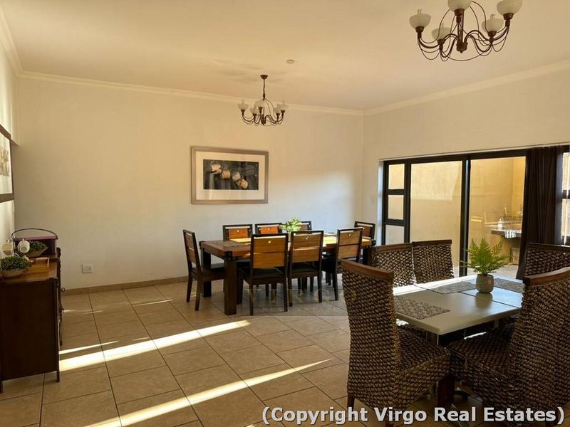 A spacious dining area featuring tiled flooring, dual ceiling chandeliers, and large sliding glass doors providing access to the outdoor patio area.