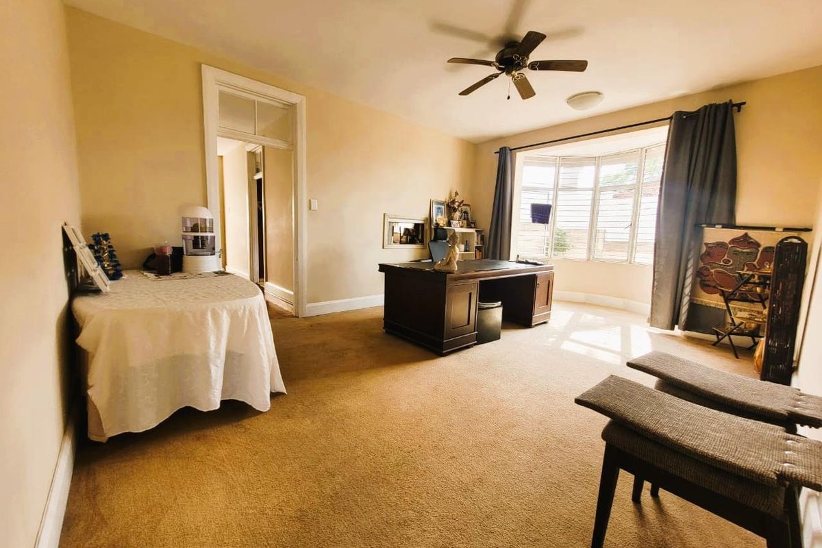 Spacious room featuring a large bay window, ceiling fan, and neutral wall finishes, currently utilized as a home office.
