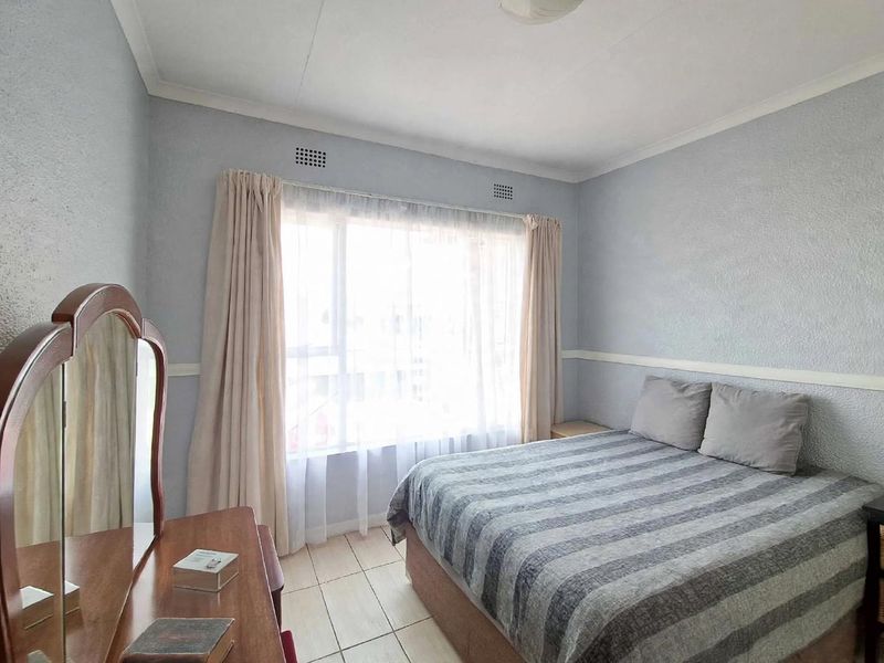 A functional bedroom featuring tiled flooring, neutral wall finishes, and a large window allowing for natural light.