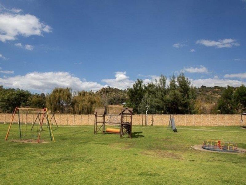A spacious communal garden area featuring a lawn, playground equipment, and a covered gazebo, enclosed by a perimeter wall.