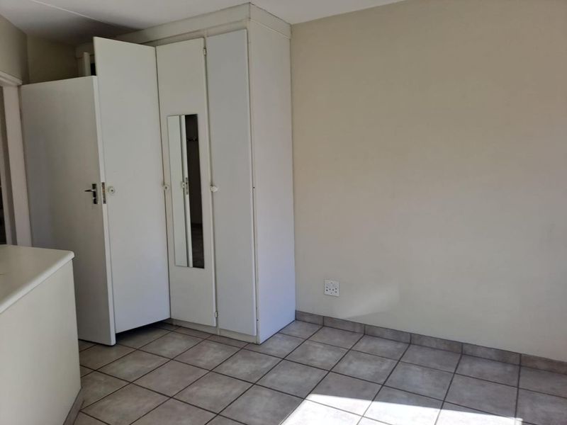 A bedroom featuring tiled flooring and built-in cupboards with a mirrored panel, offering a clean and functional space ready for personalization.