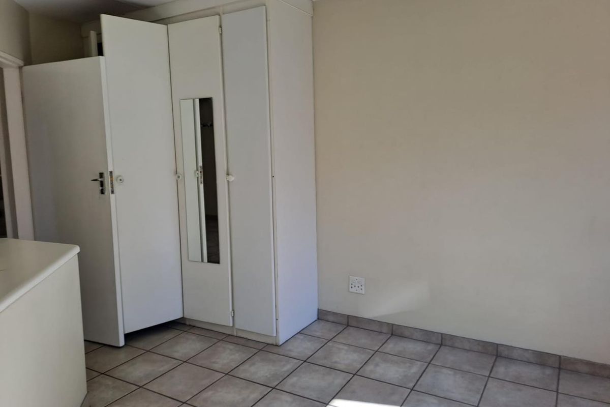 A bedroom featuring tiled flooring and built-in cupboards with a mirrored panel, offering a clean and functional space ready for personalization.