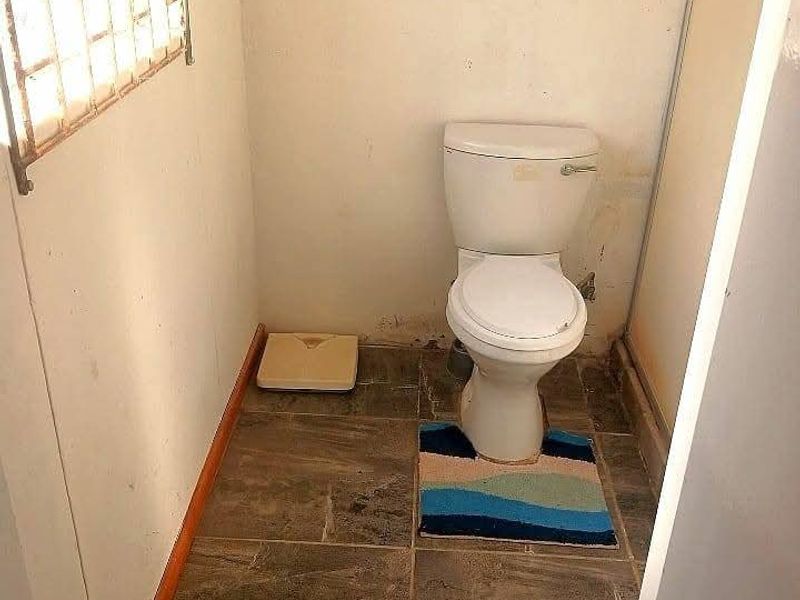 A small bathroom featuring tiled flooring, a standard toilet, and a window with security bars, requiring cosmetic updates to the wall finishes.