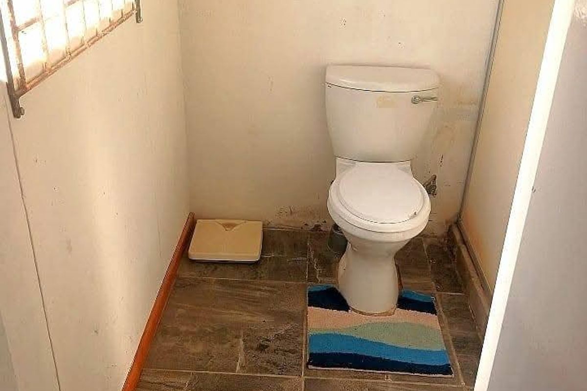 A small bathroom featuring tiled flooring, a standard toilet, and a window with security bars, requiring cosmetic updates to the wall finishes.