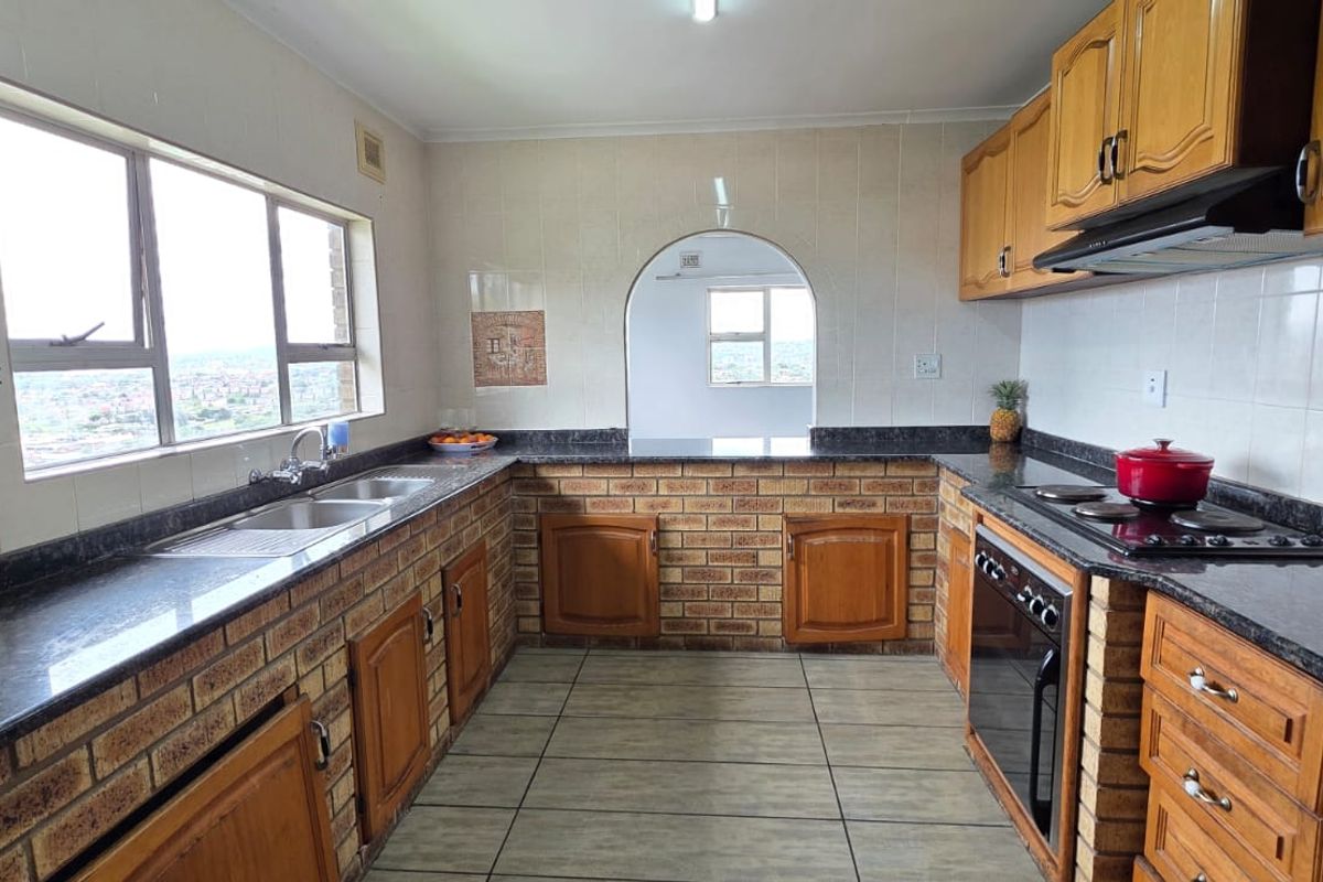 A functional kitchen featuring brick cabinetry, granite countertops, built-in oven, hob, extractor fan, and a large window with views.