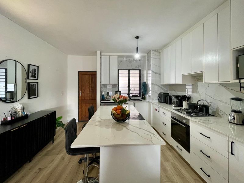 Modern kitchen featuring white cabinetry, marble-look quartz countertops, a central island, built-in oven, and gas hob, complemented by light wood-look laminate flooring.