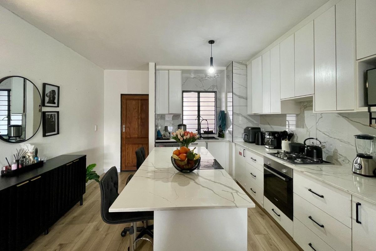 Modern kitchen featuring white cabinetry, marble-look quartz countertops, a central island, built-in oven, and gas hob, complemented by light wood-look laminate flooring.