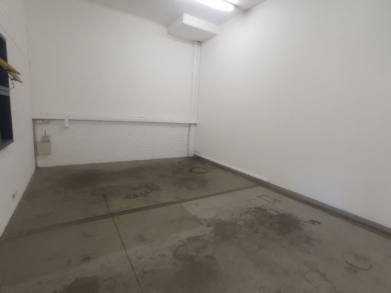 An empty, utilitarian industrial space featuring concrete flooring, exposed brick walls, and overhead fluorescent lighting, suitable for storage or workshop use.