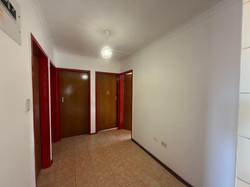 A functional hallway featuring tiled flooring, white walls, and multiple wooden doors with red-painted frames.