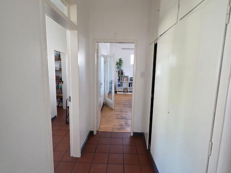 A functional hallway featuring terracotta floor tiles and extensive built-in storage cupboards, providing access to adjacent rooms with timber flooring.