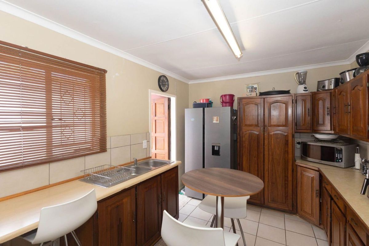A functional kitchen featuring traditional timber cabinetry, tiled flooring, a double stainless steel sink, and a breakfast bar area.